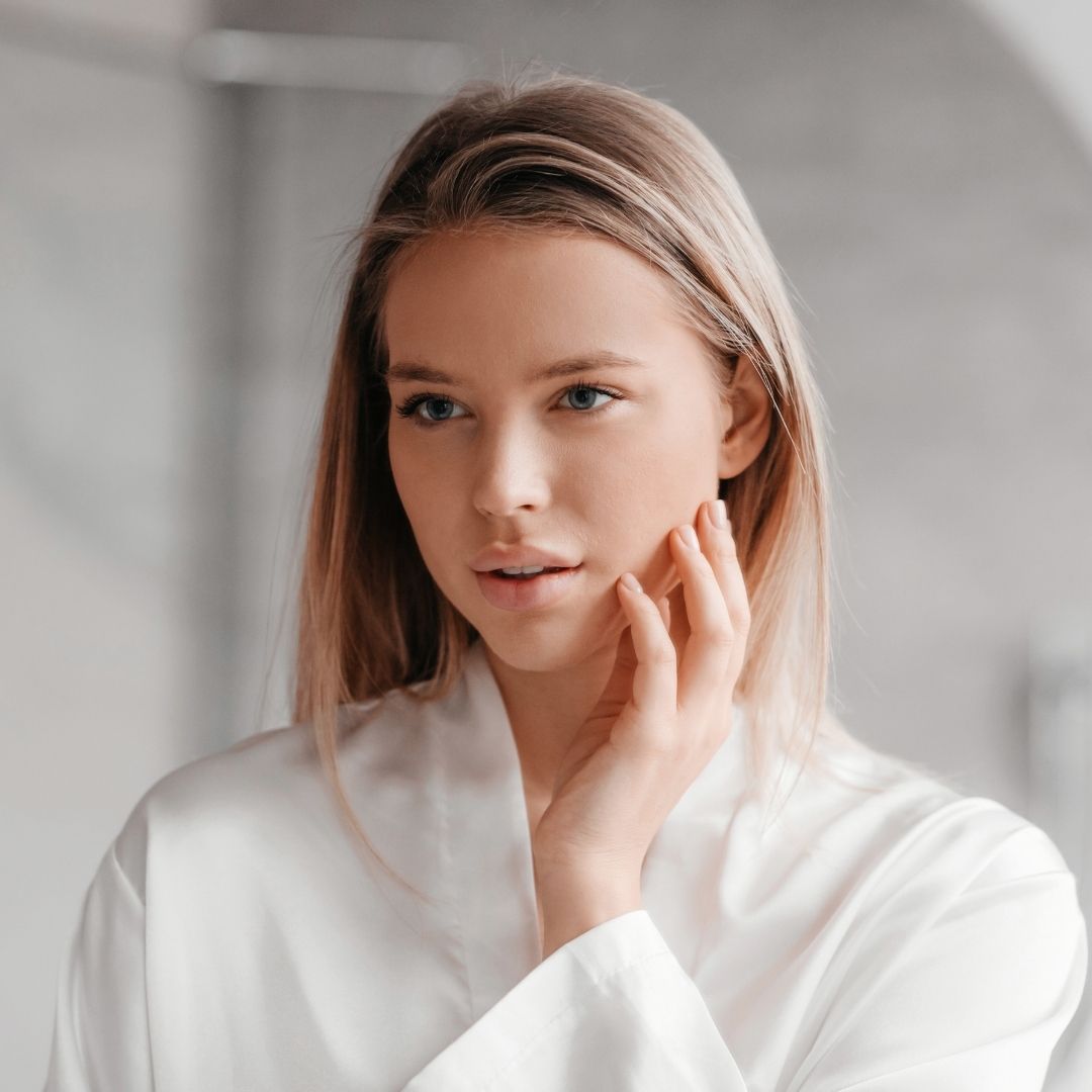 Girl in white robe in bathroom touching face