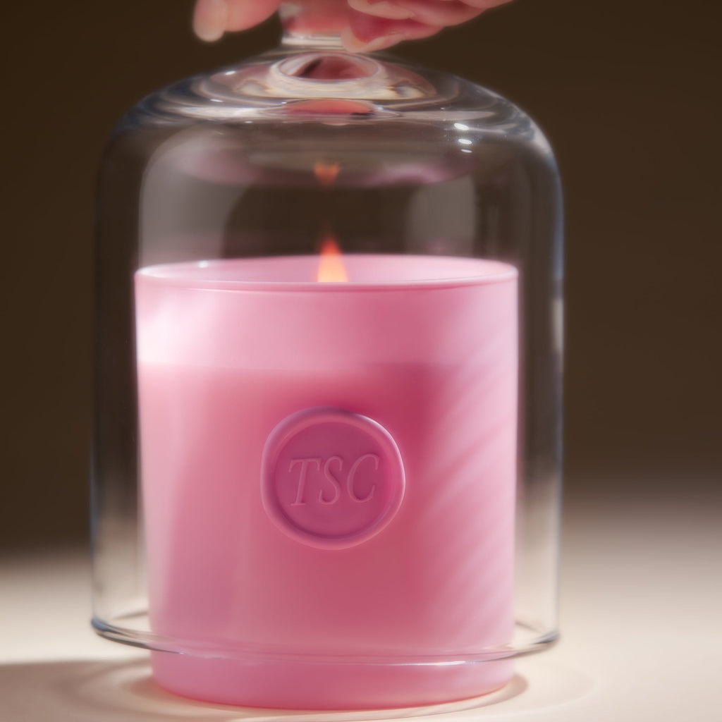 Pink candle under glass dome with flame.