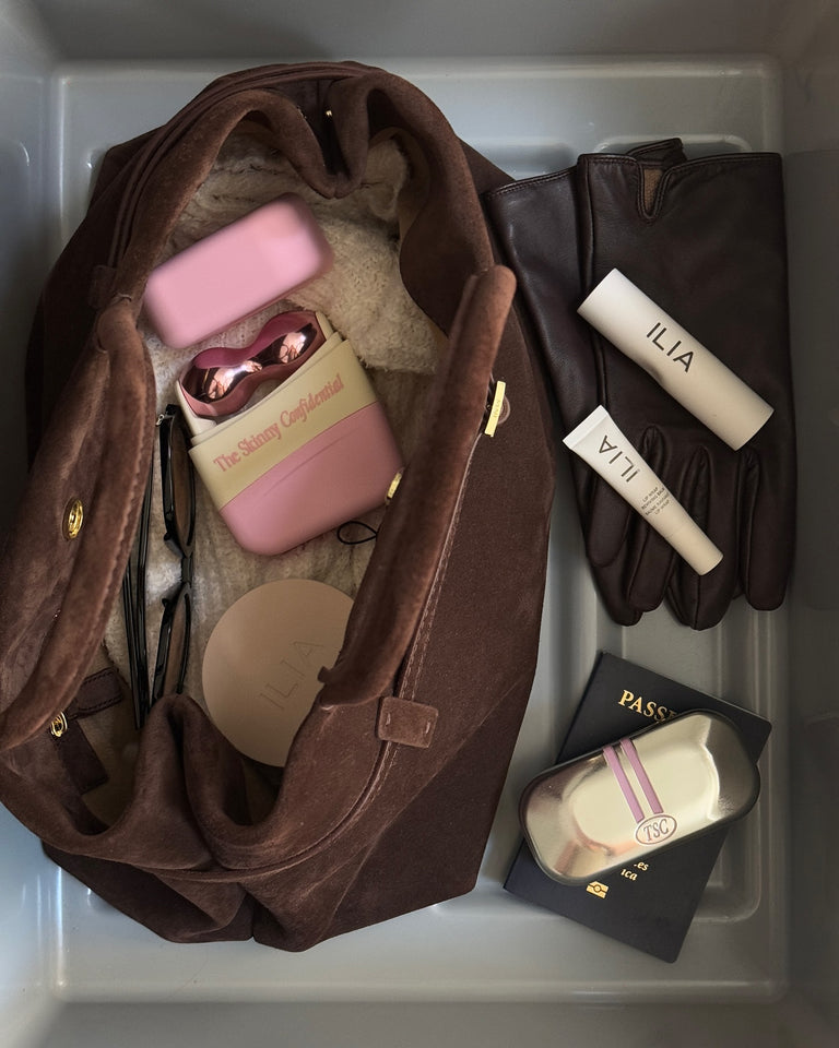 Brown handbag with beauty products, gloves, passport, and travel essentials.